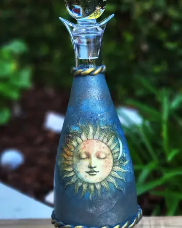 Deep blue bottle hand-painted with a golden sun face, finished with a clear faceted stopper
