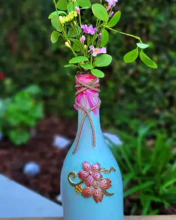 Blue vase with a sculpted pink blossom at the neck, holding fresh stems