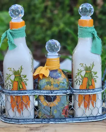 Three bottles painted with carrots and greenery, set in a wire carrier