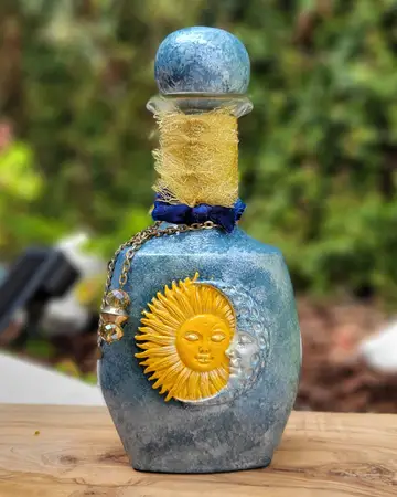 Slate blue bottle with a painted sun face and a beaded neck wrap