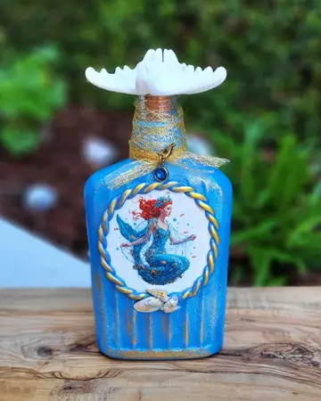 Bright blue bottle with a framed mermaid panel and gold cord