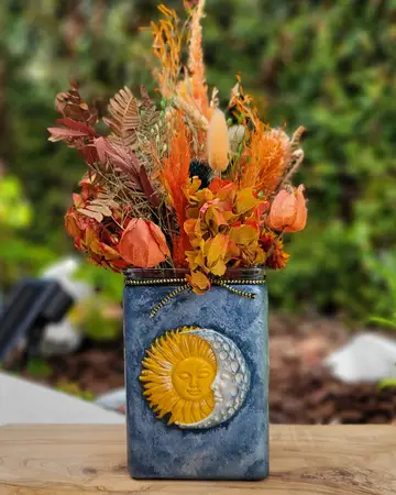 Textured vase with a sun medallion, holding a dried autumn arrangement