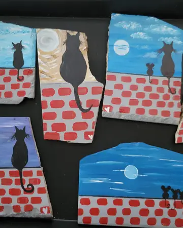 Painted tiles showing cats sitting on a red brick wall at night